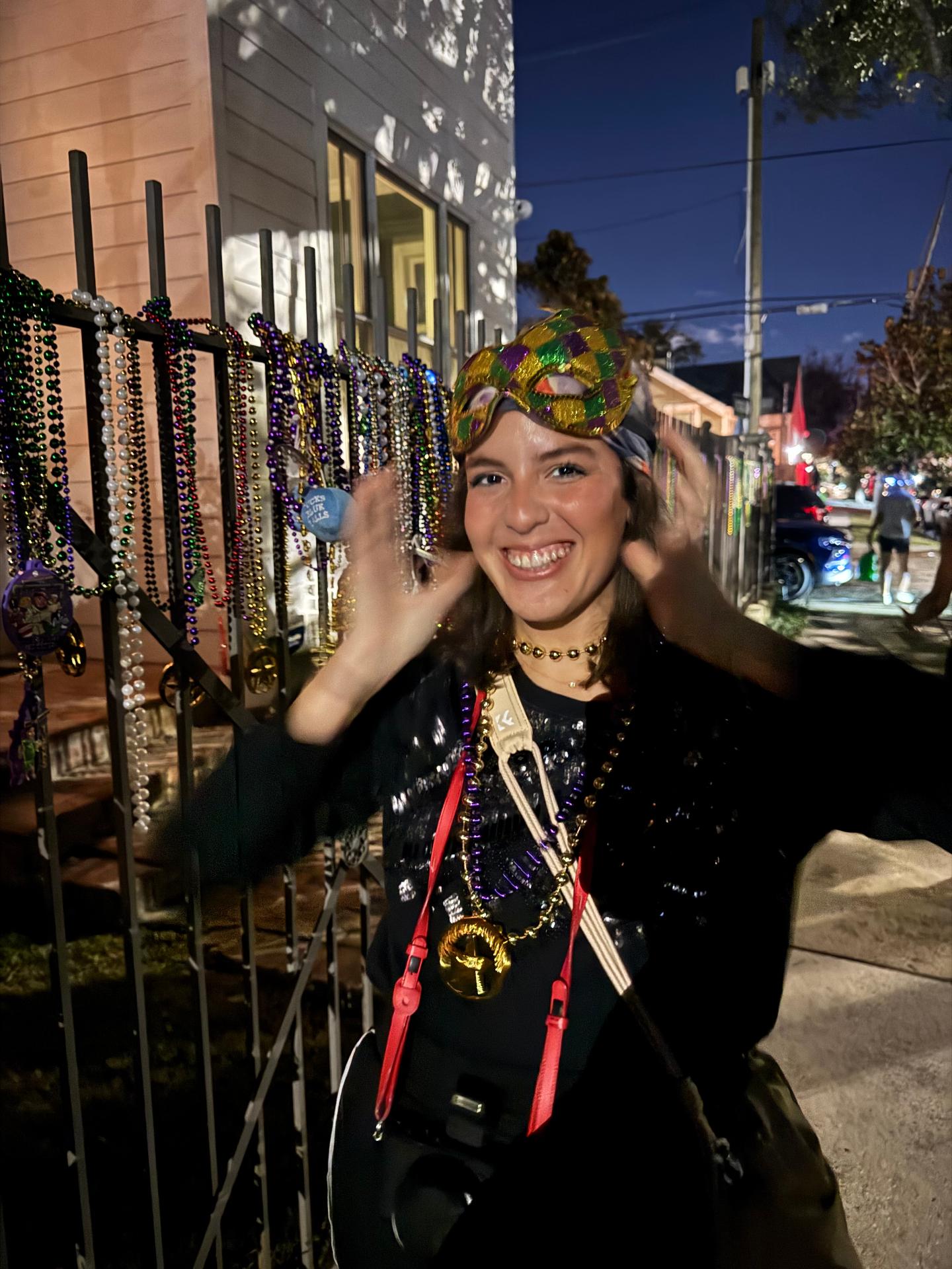 Mujer sonriendo con máscara y collares junto a una verja de noche