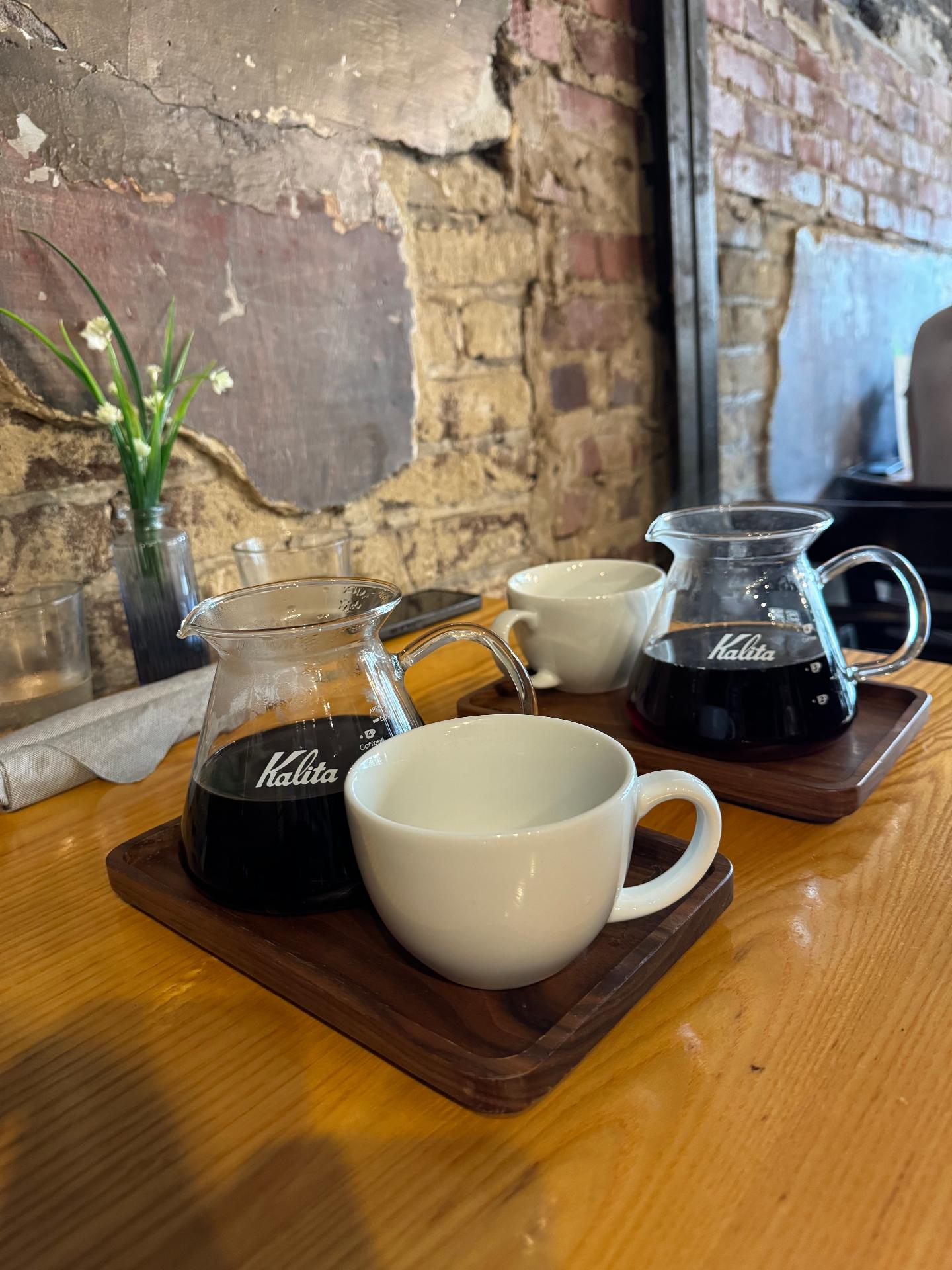 Servidores Kalita y tazas de café sobre mesa de madera